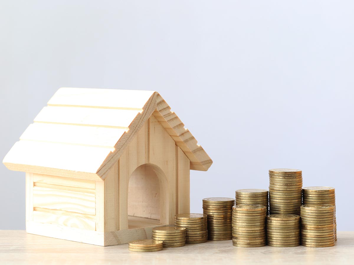 Small wooden house next to a stack of coins.