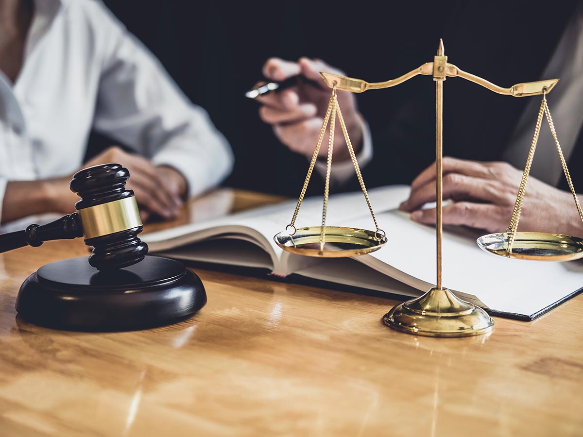 Lawyer consulting his client, with a judge’s gavel and legal scales in the foreground. 