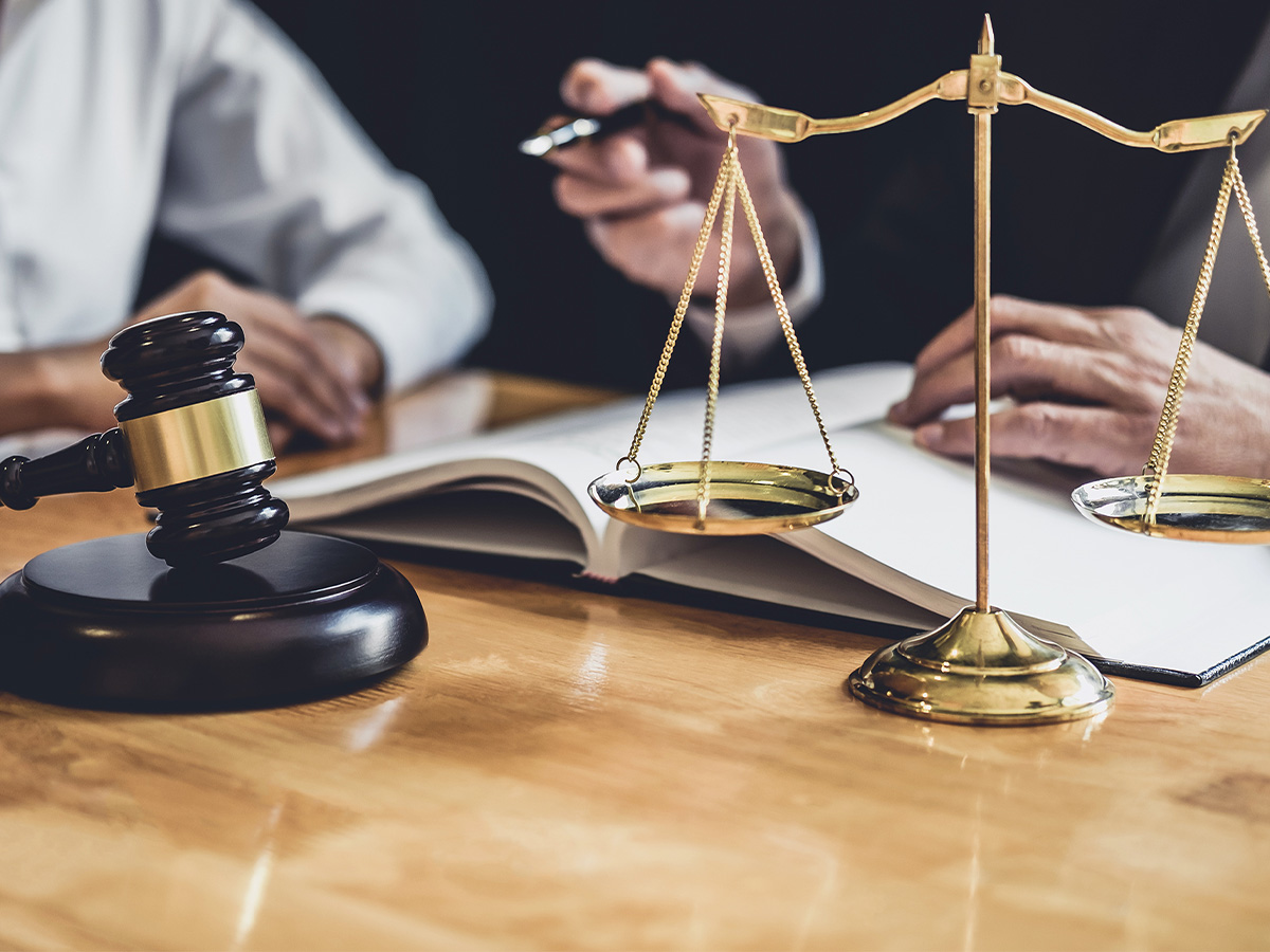 Male lawyer working with a client in a courtroom. Legal concept with legal props in the foreground. Judges gavel and scales.