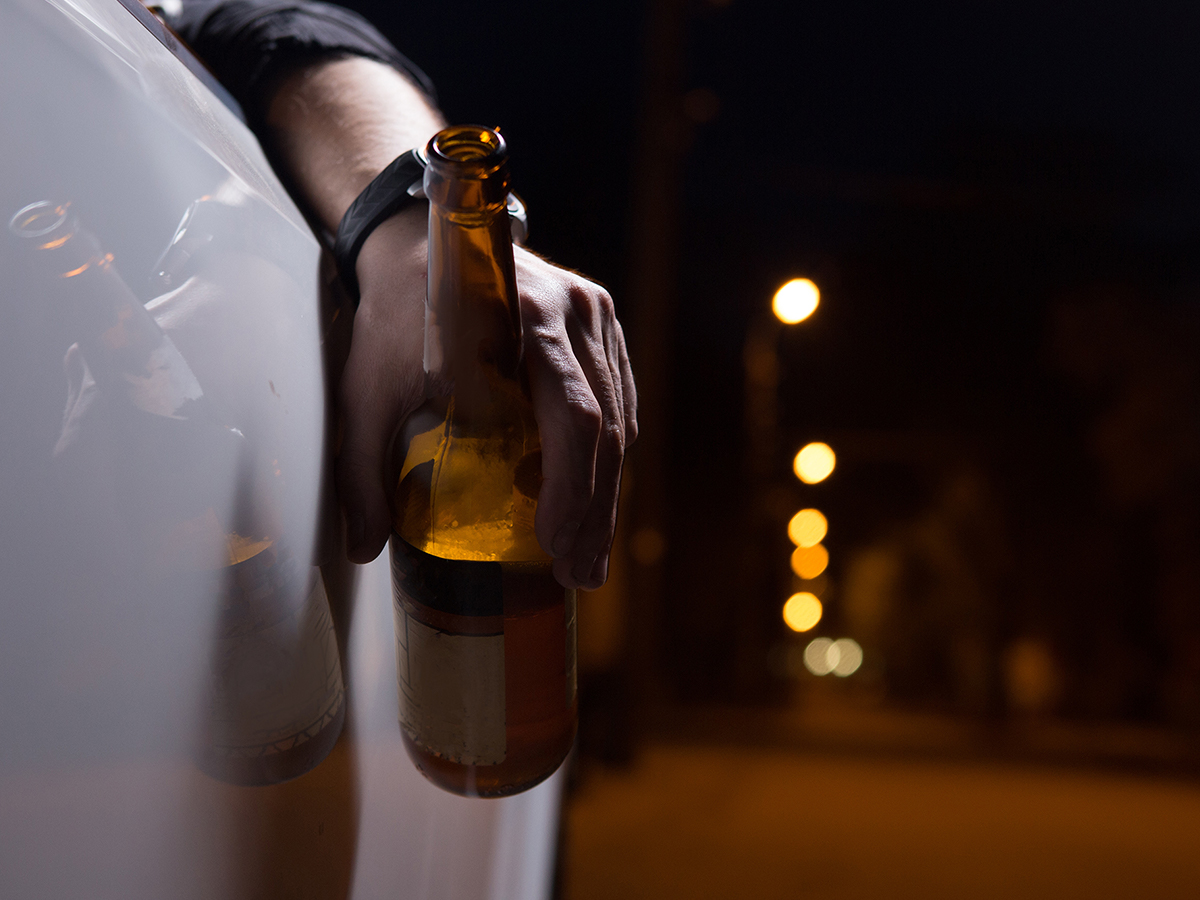 Man holding open beer bottle outside car window
