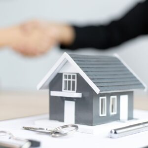 Handshakes in background with miniature house at the forefront