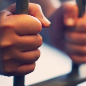 a person holding on to jail bars