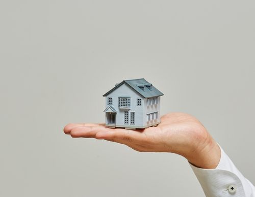A hand holding a small model house against gray.
