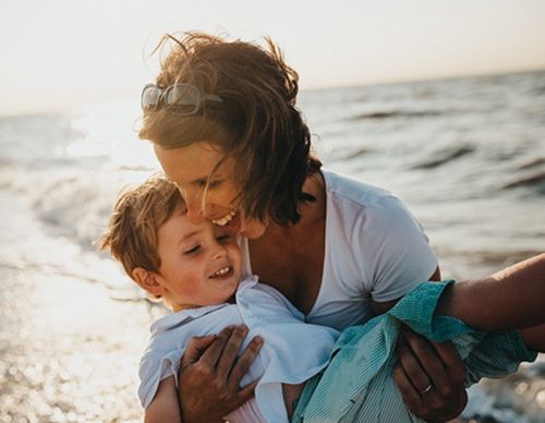 Mother laughing while holding her son at the beach.