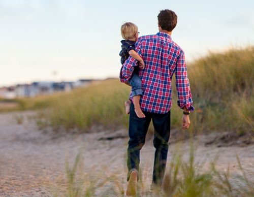 Father carrying his son across a grassy dune.