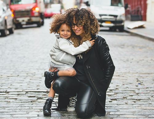 Mother crouching and hugging her daughter on city street.