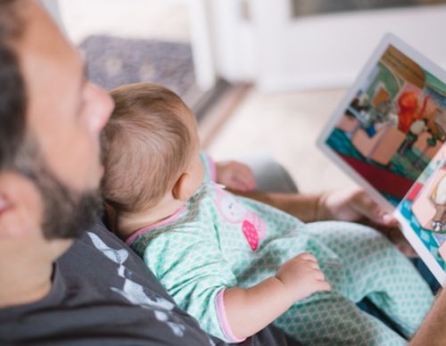 Father reading a book to a baby in pajamas.
