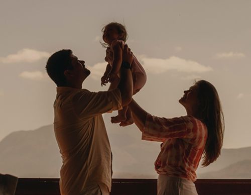 Silhouette of parents lifting their child against the sky.