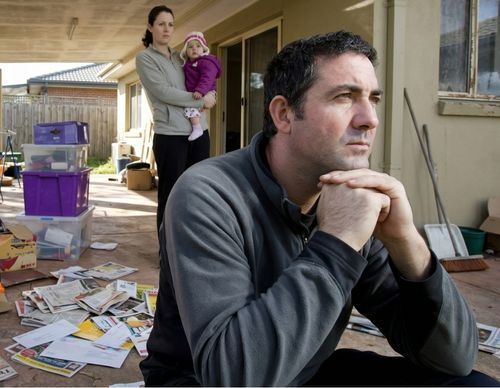 Sad man sitting outdoors near moving boxes and family.