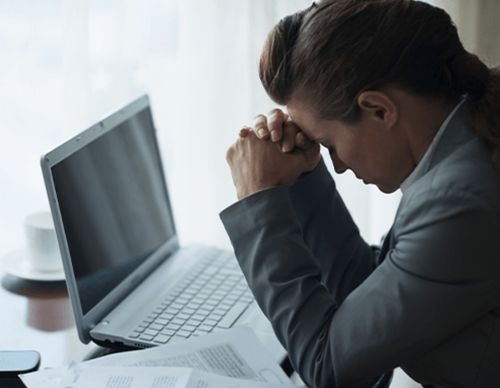 Stressed businesswoman with head in hands at a laptop.