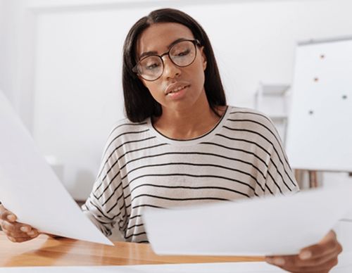 Woman with glasses carefully reading two paper documents