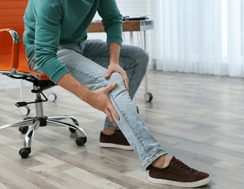Man sitting in an office chair holding an injured leg.