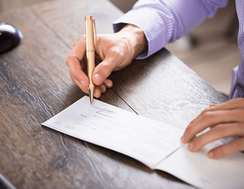 Close-up of a person signing a paper paycheck.