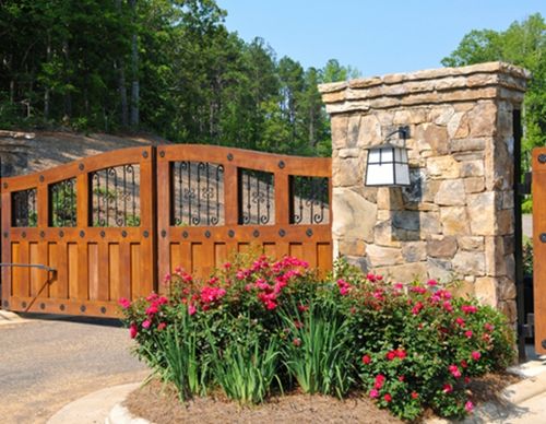 Wooden gated entrance with stone pillars and flowers.