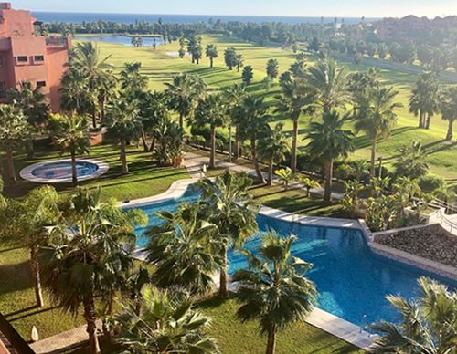 Resort pool area with palm trees and golf course.
