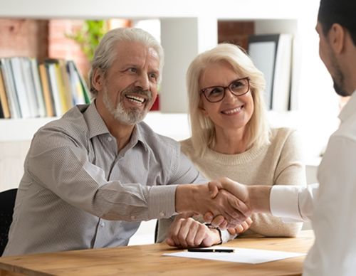 Senior couple smiling while shaking hands with a lawyer.