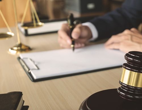 Legal professional signing a document behind a gavel.