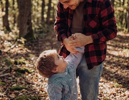 Man in flannel shirt holding a toddler's hands outdoors.