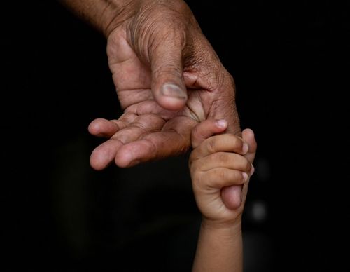 A small child's hand gripping an adult's finger.