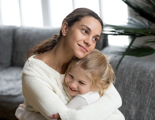Smiling mother embracing her young daughter on a sofa.