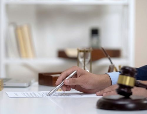 A hand signing a legal document next to a gavel.