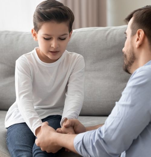 A father holding his son's hands on a couch.