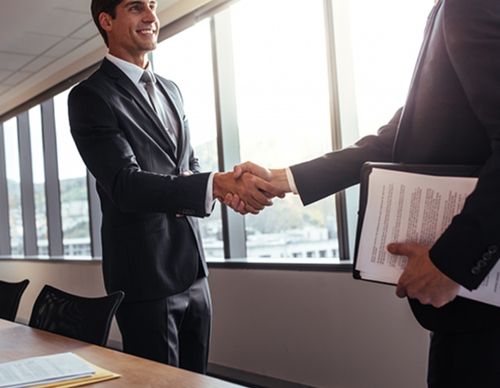 Two businessmen shaking hands in a sunlit office.