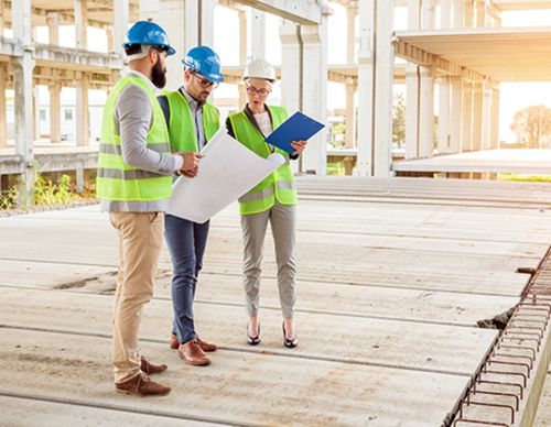 Three engineers in safety gear discussing blueprints onsite