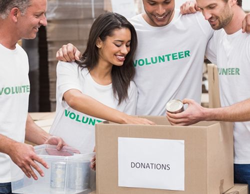 Volunteers smiling while packing a donation box.
