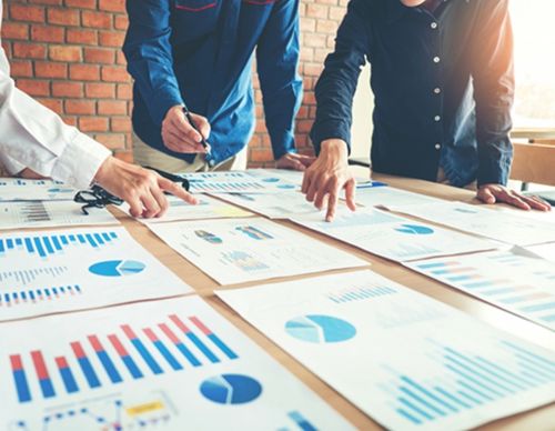 Hands pointing at colorful data charts on a table.