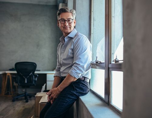Smiling businessman leaning against a window in a studio.