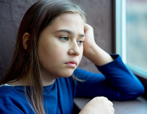 Young girl with a tear on her cheek looking out window