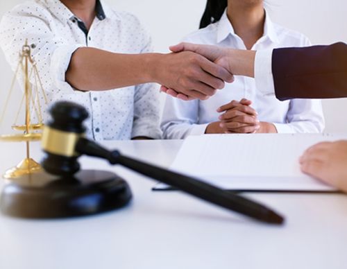 Shaking hands in front of a gavel and scales.