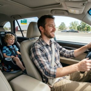 A dedicated father driving safely while his young child sits happily strapped in a secure back seat car seat.