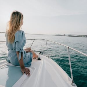 A woman sitting on the bow of a moving yacht looking out at the coastline, highlighting recreational boating legal protection.